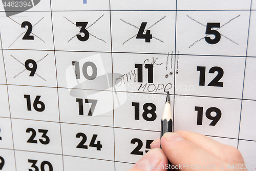 Image of The hand with a pencil writes the words vacation and sea on a wall calendar