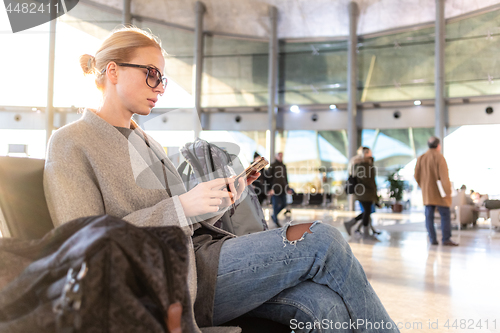 Image of Female traveler using her cell phone while waiting to board a plane at departure gates at airport terminal.