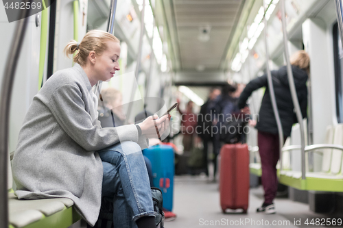 Image of Beautiful blonde woman wearing winter coat reading on the phone while traveling by metro public transport.