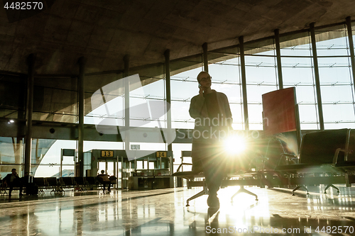 Image of Female traveler talking on her cell phone while waiting to board a plane at departure gates at airport terminal.