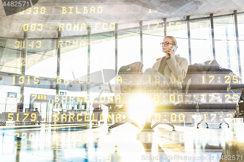 Image of Female traveler talking on her cell phone while waiting to board a plane at departure gates at airport terminal.