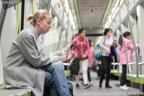 Image of Beautiful blonde woman using smart phone while traveling by metro public transport.