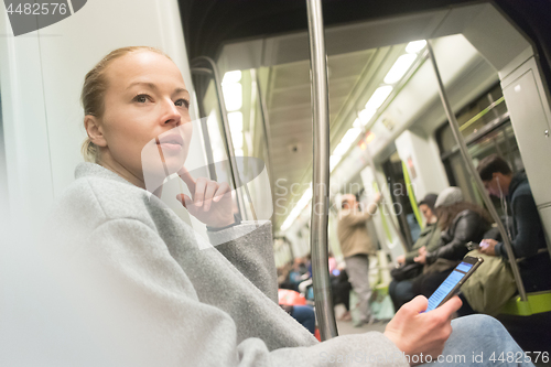 Image of Beautiful blonde woman using smart phone while traveling by metro public transport.