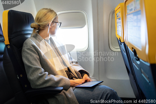 Image of Thoughtful woman looking through the window while traveling by airplane.