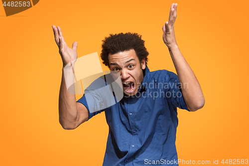 Image of The young emotional angry man screaming on orange studio background