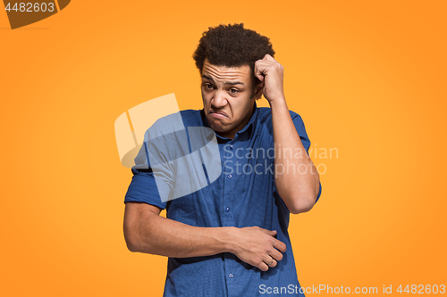 Image of Let me think. Doubtful pensive man with thoughtful expression making choice against orange background