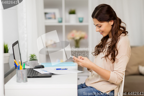Image of woman with papers and smartphone working at home