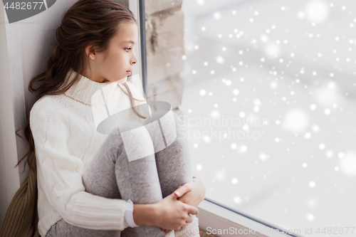 Image of sad girl sitting on sill at home window in winter