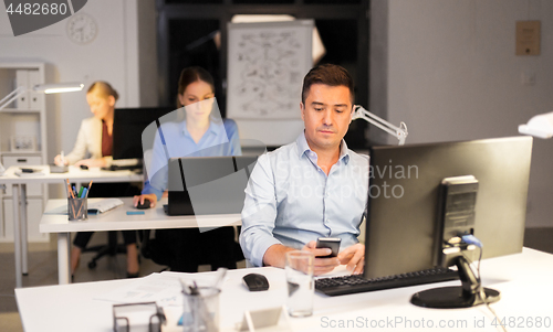 Image of man with smartphone working at night office