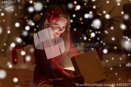 Image of smiling girl opening christmas gift at night