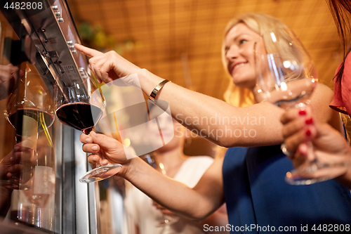 Image of happy women pouring wine from dispenser at bar