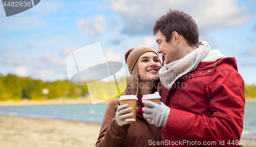 Image of happy couple with coffee cups over autumn beach