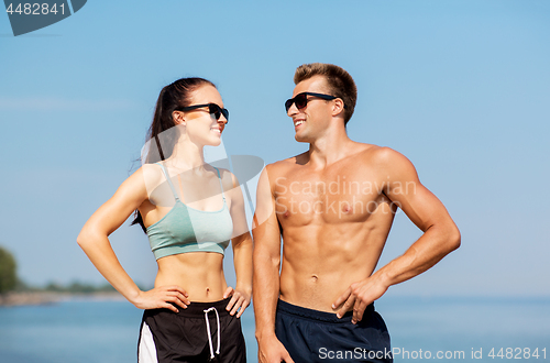 Image of happy couple in sports clothes and shades on beach