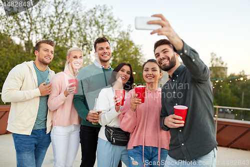 Image of friends with drinks taking selfie at rooftop party