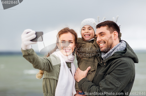 Image of family taking selfie by smartphone on autumn beach