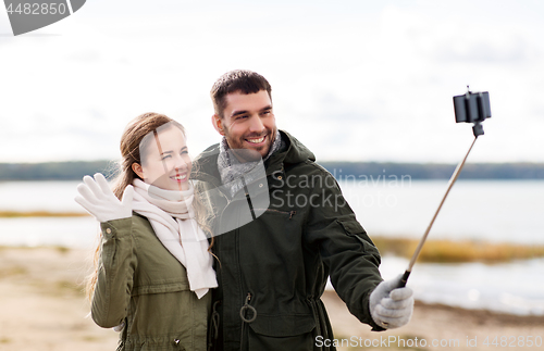 Image of happy couple taking selfie on beach in autumn
