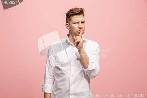 Image of The young man whispering a secret behind her hand over pink background