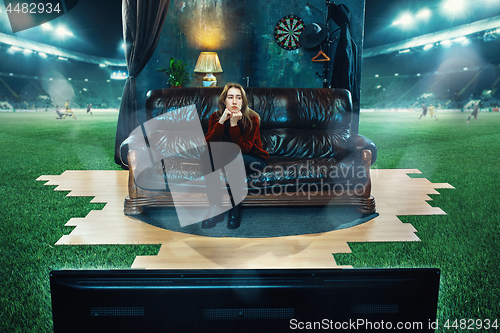 Image of Boring fan is sitting on the sofa and watching TV in the middle of a football field.