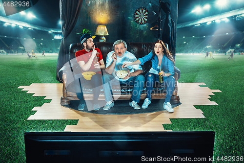 Image of Ardent fans are sitting on the sofa and watching TV in the middle of a football field.