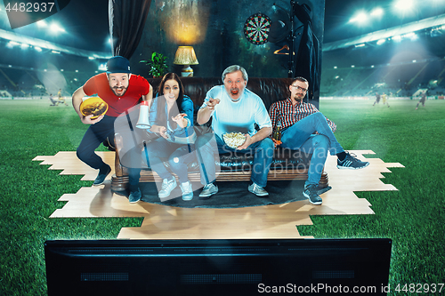 Image of Ardent fans are sitting on the sofa and watching TV in the middle of a football field.