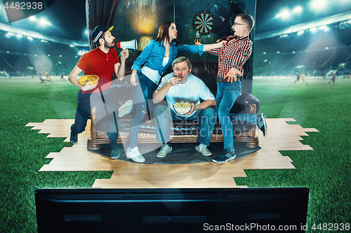 Image of Ardent fans are sitting on the sofa and watching TV in the middle of a football field.