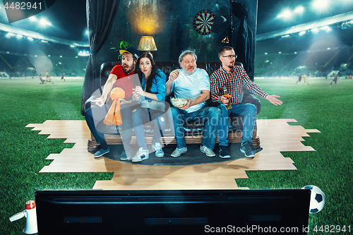 Image of Ardent fans are sitting on the sofa and watching TV in the middle of a football field.