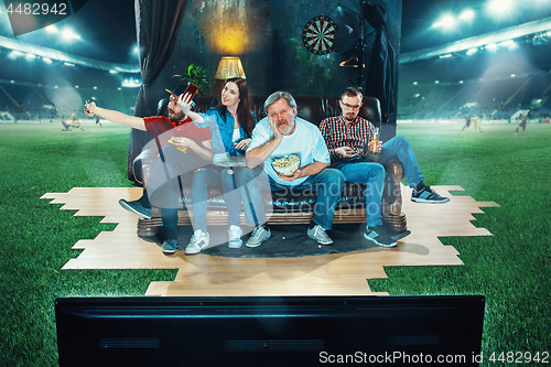 Image of Ardent fans are sitting on the sofa and watching TV in the middle of a football field.