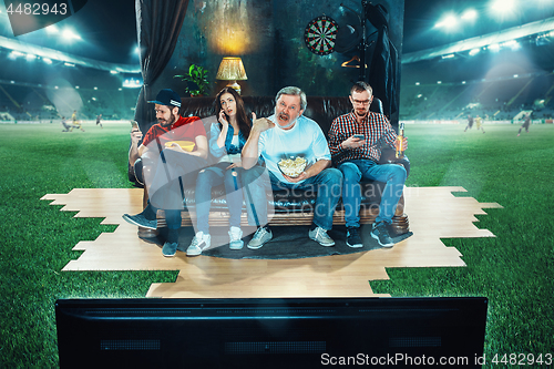 Image of Ardent fans are sitting on the sofa and watching TV in the middle of a football field.