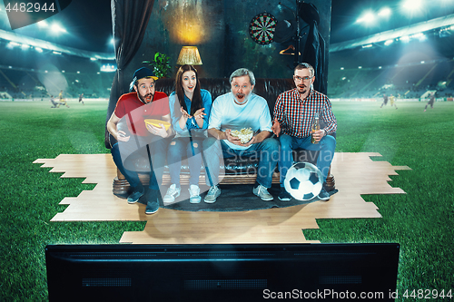 Image of Ardent fans are sitting on the sofa and watching TV in the middle of a football field.