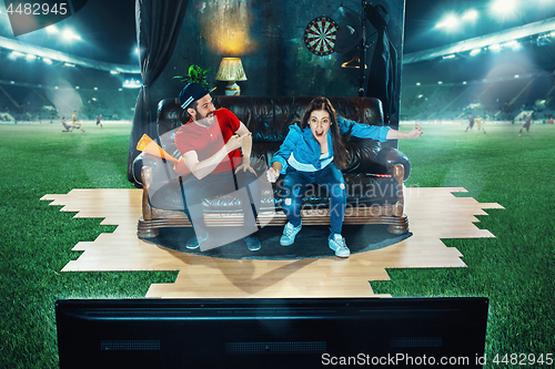 Image of Ardent fans are sitting on the sofa and watching TV in the middle of a football field.