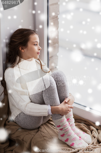 Image of sad girl sitting on sill at home window in winter