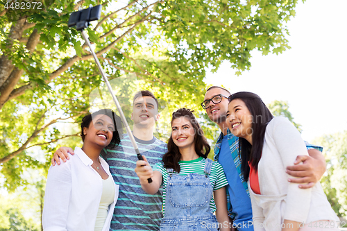 Image of happy friends taking photo by selfie stick at park