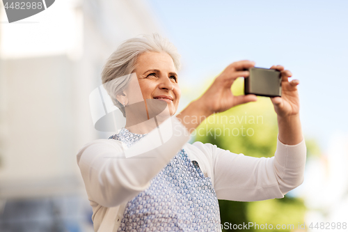 Image of senior woman photographing by smartphone in city