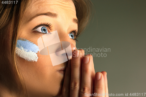 Image of Portrait of a woman with the flag of the Argentina painted on her face.