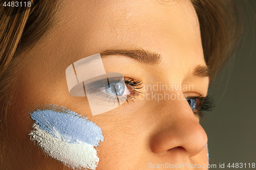 Image of Portrait of a woman with the flag of the Argentina painted on her face.