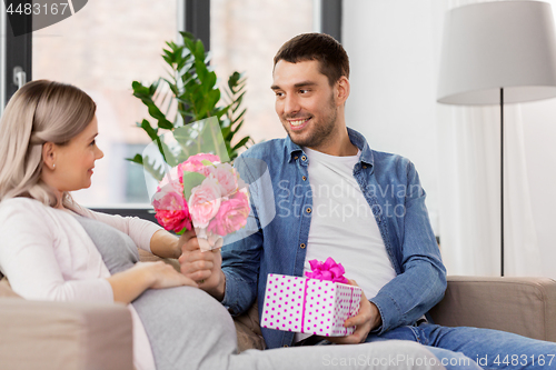 Image of man giving flowers to pregnant woman at home