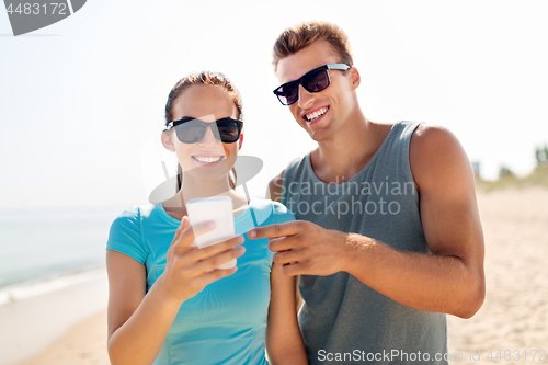 Image of couple in sports clothes with smartphones on beach