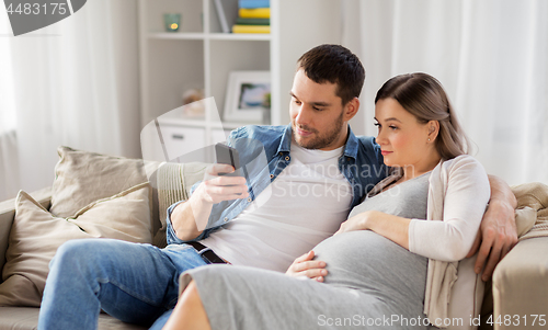 Image of man and pregnant wife with smartphone at home