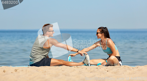 Image of smiling couple stretching legs on beach