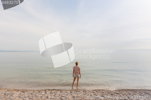 Image of Happy Carefree Woman Enjoying Sunset Walk on White Pabbled Beach.