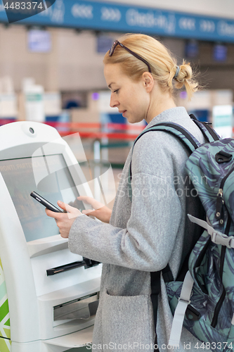 Image of Casual caucasian woman using smart phone application and check-in machine at the airport getting the boarding pass.