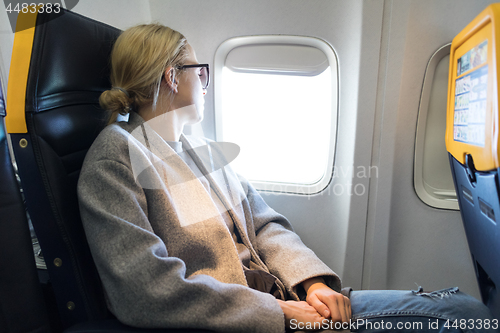 Image of Thoughtful woman looking through the window while traveling by airplane.