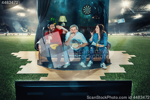 Image of Ardent fans are sitting on the sofa and watching TV in the middle of a football field.