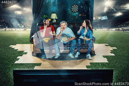 Image of Ardent fans are sitting on the sofa and watching TV in the middle of a football field.