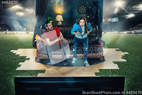 Image of Ardent fans are sitting on the sofa and watching TV in the middle of a football field.