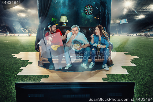 Image of Ardent fans are sitting on the sofa and watching TV in the middle of a football field.