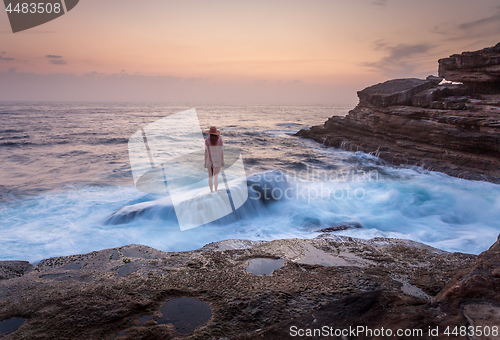 Image of Female standing on shipwreck rock with ocean flowing over it