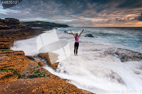 Image of Girl standing on rocks as ocean waves wash past her feet