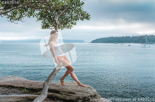 Image of Female sitting by the seashore on the curved trunk of a tree