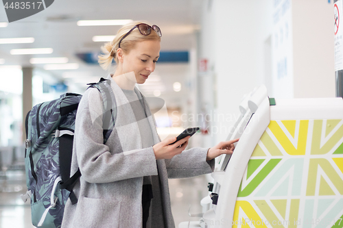 Image of Casual caucasian woman using smart phone application and check-in machine at the airport getting the boarding pass.